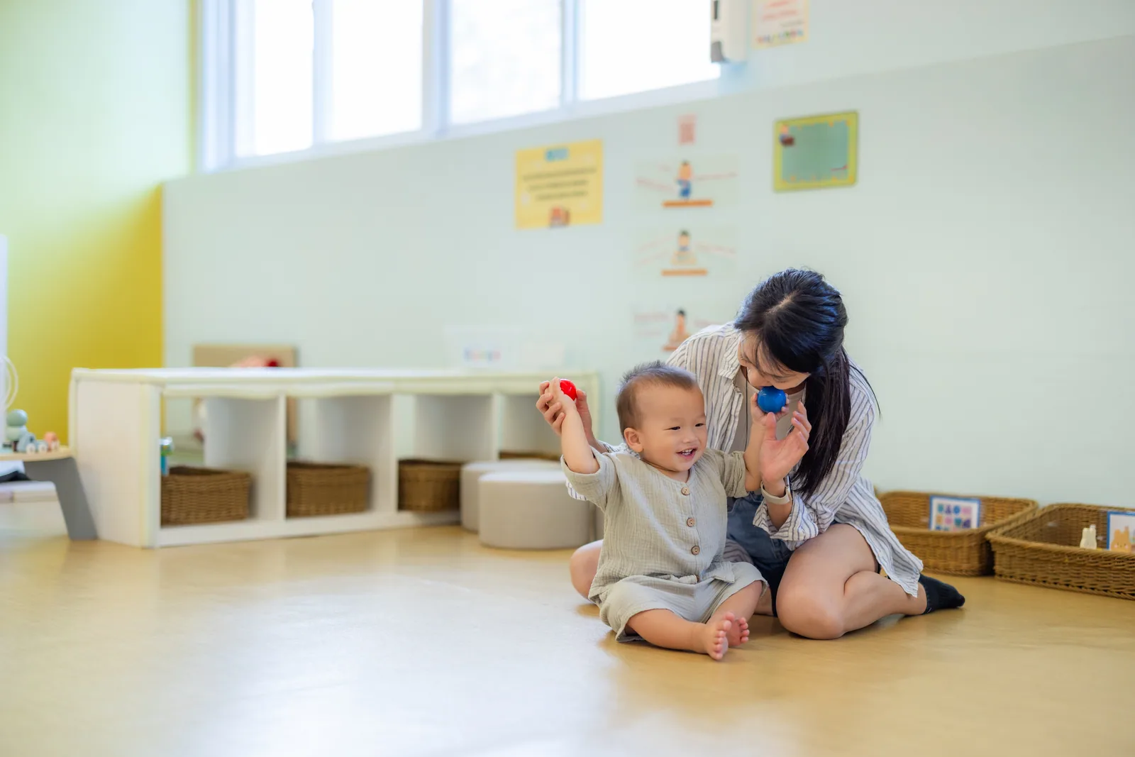 A teacher sitting on the floor of a bright, calm classroom, playing with a toddler