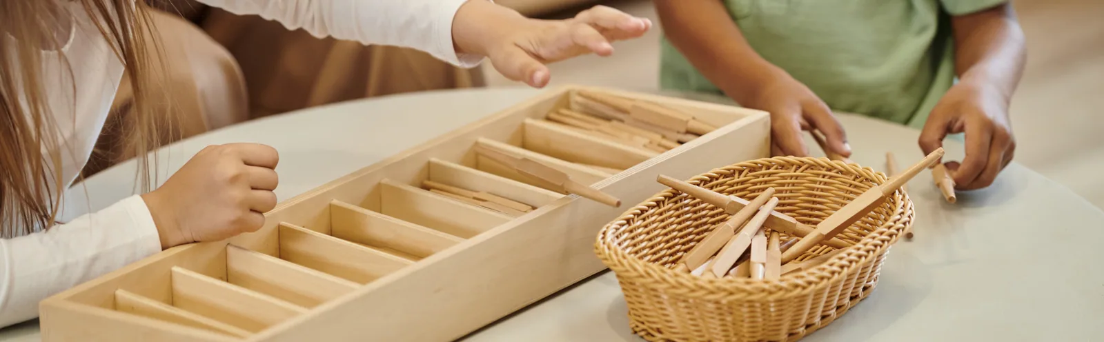 Small hands sorting wooden pieces into a divided tray beside a woven basket