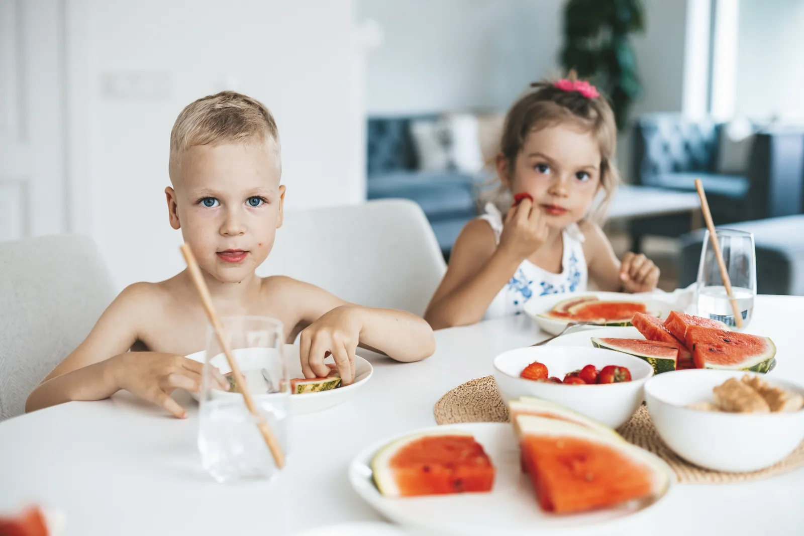 Two young children at a table set with bowls of watermelon and strawberries