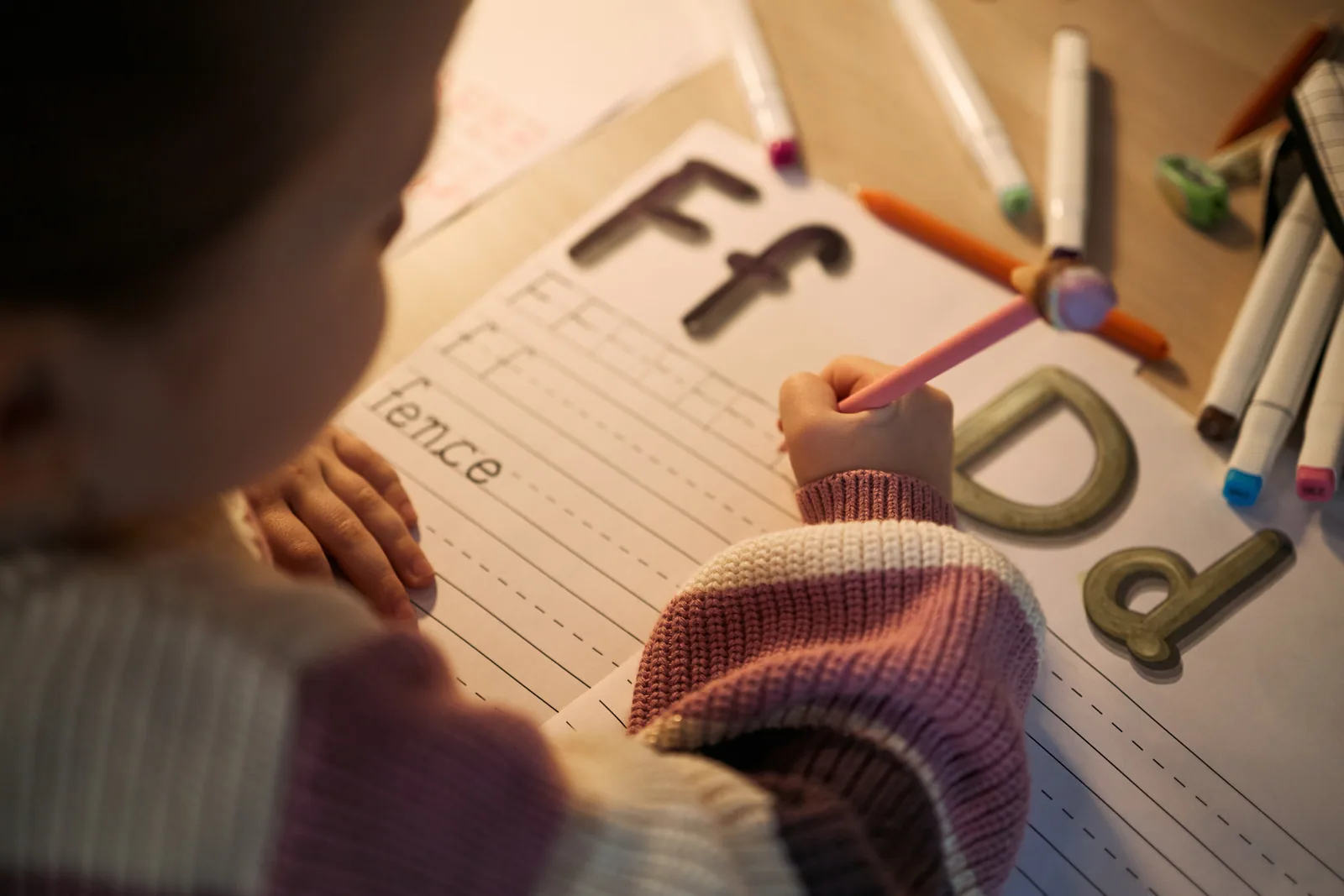A child practicing letters on lined paper beside wooden letter shapes