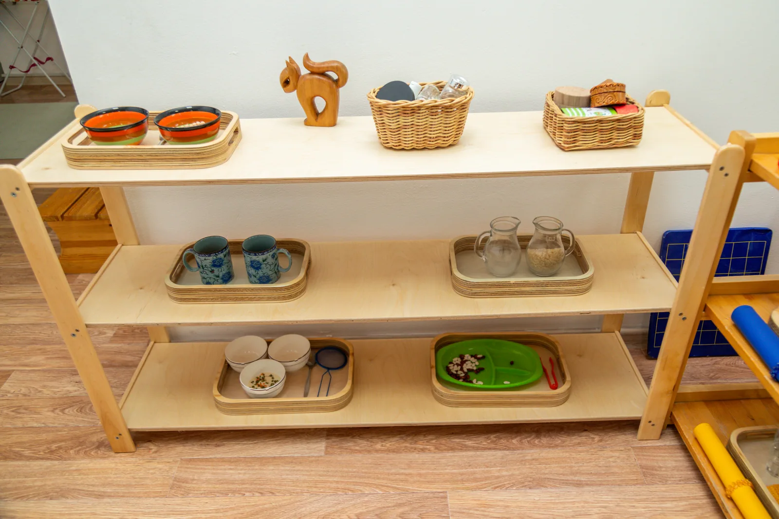 Wooden classroom shelves holding trays and baskets of learning materials